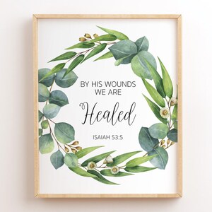 Può includere: Una stampa incorniciata bianca con una ghirlanda di eucalipto verde e il testo "Dalle sue ferite siamo guariti" con il riferimento biblico "Isaia 53:5".