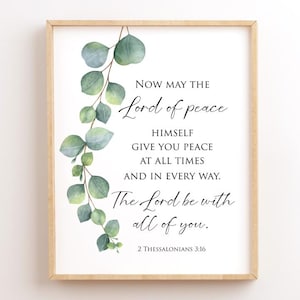 May include: A printable wall art design with a white background and a black text quote from the Bible, 2 Thessalonians 3:16. The quote reads "Now may the Lord of peace himself give you peace at all times and in every way. The Lord be with all of you." The text is surrounded by a watercolor illustration of eucalyptus leaves.