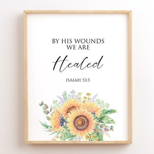 May include: A framed print with a white background and a floral design. The text reads "By His Wounds We Are Healed" with the scripture reference "Isaiah 53:5" below.