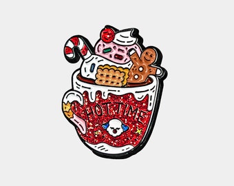 May include: A festive enamel pin in the shape of a red glittery mug filled with whipped cream, a gingerbread man, and a candy cane. The mug has the words "HOT TIME" and a skull graphic.