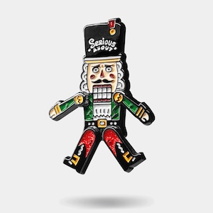 May include: A black, green, and red nutcracker figurine with a white face and a red hat. The nutcracker is wearing a green jacket and red pants. The nutcracker is holding a red and white candy cane in its right hand. The nutcracker has a serious expression on its face. The text "Serious About" is written on the hat.