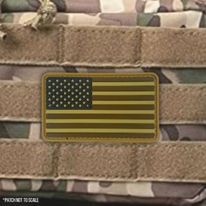 May include: A brown and tan American flag patch with a velcro backing. The patch is on a camouflage background.
