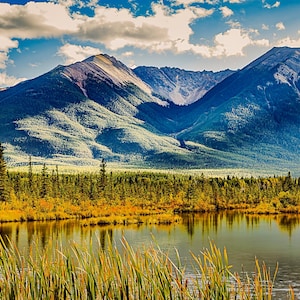 Peut inclure: Une vue panoramique d'une chaîne de montagnes avec un lac au premier plan. Les montagnes sont couvertes d'arbres et ont une teinte bleue. Le lac est calme et reflète le ciel et les montagnes.