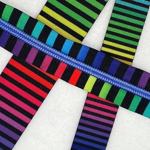 May include: Close-up of colourful striped zipper tape in a rainbow of colours, including red, orange, yellow, green, blue, and purple. The zipper tape has a black background with horizontal stripes. A blue zipper is visible.