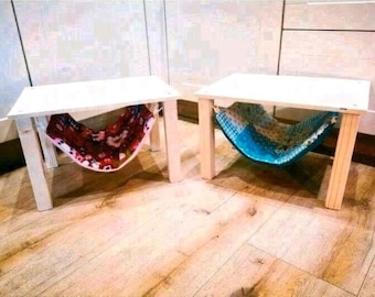 May include: Two wooden tables with fabric hammocks hanging underneath. The table on the left has a pink and red patterned hammock, while the table on the right has a blue and white patterned hammock.