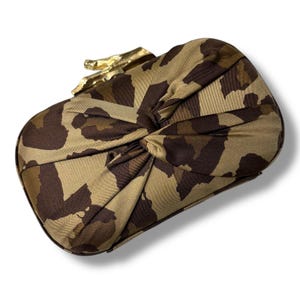 May include: A rectangular clutch with a tan and brown leopard print pattern. The clutch has a gold-colored clasp and a knotted design on the front. The bag is approximately 10 inches long and 6 inches high.
