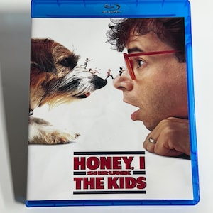 May include: Blu-ray disc case for the movie "Honey, I Shrunk the Kids." The cover features a dog and a man with red glasses looking at each other, with tiny people in between. The title is in red and white text.