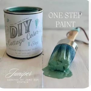 May include: A green paint can with the text "DIY Cottage Colors" and "One Step" on the label. The paint is labeled "Juniper" and is curated by Jami Ray Vintage. A paintbrush with green paint on it is in the foreground.