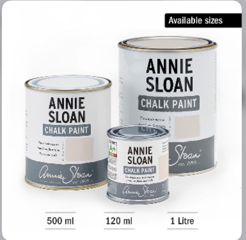 Może przedstawiać: Trzy puszki farby kredowej Annie Sloan w r&oacute;żnych rozmiarach: 120 ml, 500 ml i 1 litr. Puszki są białe z czarnym nadrukiem i logo Annie Sloan.