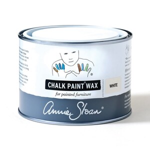 May include: A white can of Annie Sloan Chalk Paint Wax for painted furniture. The can has a hand-painted design of a person with colorful hands. The text on the can reads "Chalk Paint Wax" and "for painted furniture".