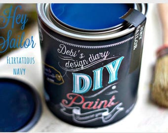 May include: A can of navy blue DIY paint with the text "Hey Sailor" and "Flirtatious Navy". The can has a black label with white and teal lettering that reads "Debi's design diary DIY Paint". A paint brush is in the background.