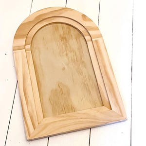 May include: A wooden frame with an arched opening, perfect for displaying photos or artwork. The frame is made of natural wood and has a rustic, farmhouse style.