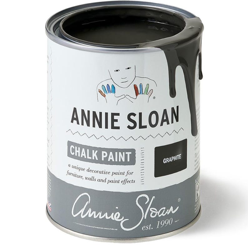 May include: A can of Annie Sloan Chalk Paint in the color Graphite. The can is white with black text and a black and white illustration of hands. The can is partially open and the paint is dripping down the side.