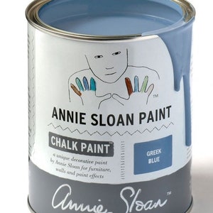 May include: A can of Annie Sloan Chalk Paint in the color Greek Blue. The can is open and the paint is spilling out. The label says "Annie Sloan Chalk Paint" and "Greek Blue".