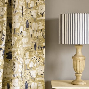 May include: A close-up of a fabric curtain with a white and blue abstract pattern. The curtain is hanging in front of a light gray wall. A lamp with a striped lampshade is on a white nightstand. The lampshade is white with blue stripes. The nightstand is white with a drawer. The text "Annie Sloan" is written in black on the wall.