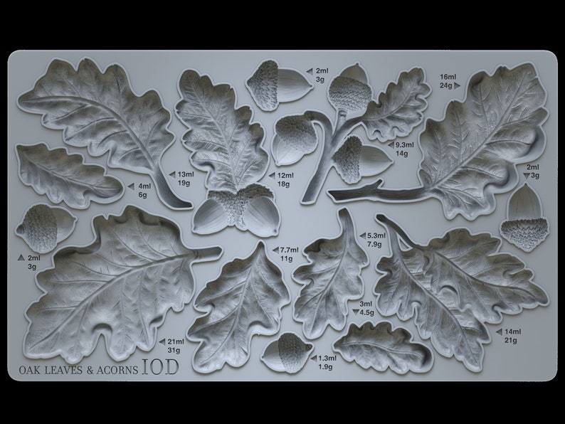 May include: A silicone mold for baking featuring oak leaves and acorns. The mold is gray and has measurements in milliliters and grams for each leaf and acorn shape. The text "OAK LEAVES & ACORNS IOD" is printed on the bottom of the mold.