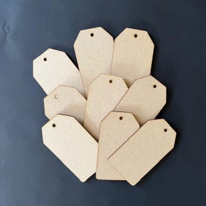 May include: A set of ten blank, unfinished, wooden gift tags with a hole punched at the top. The tags are in a natural wood color and are arranged in a fan shape.