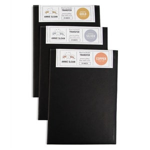May include: Three black envelopes with labels for Annie Sloan Metal Leaf Transfer in gold, silver, and copper. Each label features a hand holding a leaf and the text "Metal Leaf Transfer" and "Annie Sloan".