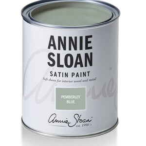 May include: A cylindrical can of Annie Sloan Satin Paint in Pemberley Blue. The can is white with black text that reads "Annie Sloan" and "Satin Paint." The paint inside is a muted blue-green color. The label also states "Soft sheen for interior wood and metal."