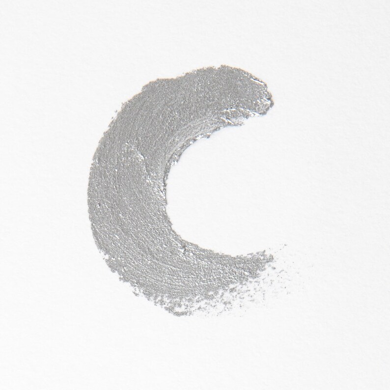 Puede incluir: Un trazo de pintura plateado en forma de media luna sobre un fondo blanco.