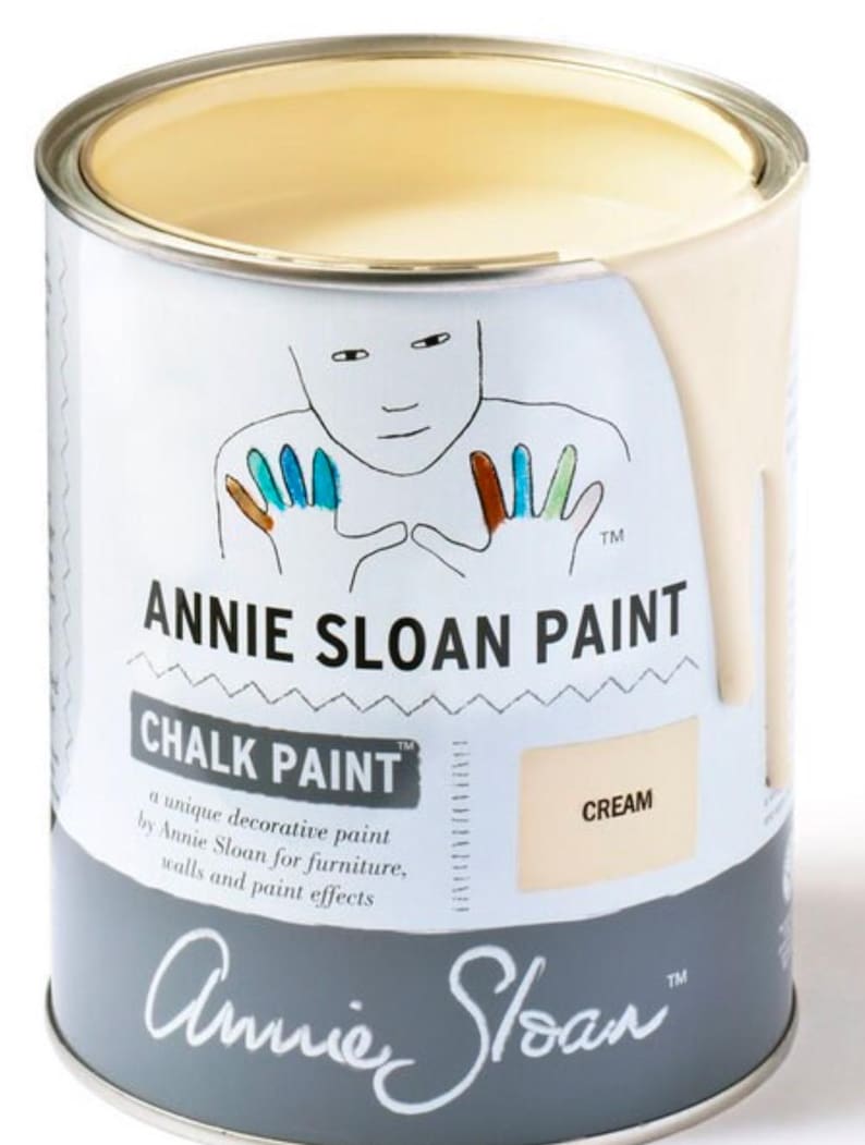 May include: A can of Annie Sloan Chalk Paint in the color Cream. The can is gray with a white label and features a handprint design. The label reads "Annie Sloan Paint" and "Chalk Paint".