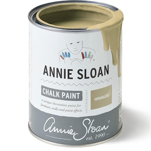 May include: A can of Annie Sloan Chalk Paint in the color Versailles. The paint is a light beige color and is shown with a small amount of paint dripping down the side of the can. The can has a white label with the Annie Sloan logo and the words "Chalk Paint" and "Versailles".