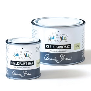 May include: Two cans of Annie Sloan Chalk Paint Wax, one large and one small. Both cans are silver with a white label. The label features a child's hand with painted fingers and the text "Chalk Paint Wax for painted furniture". The smaller can says "Clear" and the larger can says "Clear".