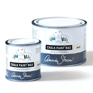 May include: Two cans of Annie Sloan Chalk Paint Wax in white. The smaller can is in the foreground and the larger can is in the background.