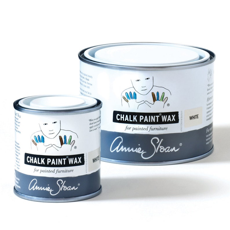 May include: Two cans of Annie Sloan Chalk Paint Wax in white. The smaller can is in the foreground and the larger can is in the background.