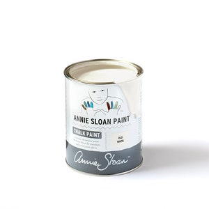 May include: A white can of Annie Sloan Chalk Paint in the color Old White. The can has a label with a hand-drawn illustration of a person with colorful fingertips. The label also includes the text "Annie Sloan Paint Chalk Paint" and "Old White".