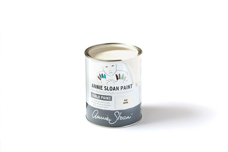 May include: A white can of Annie Sloan Chalk Paint in the color Old White. The can has a label with a hand-drawn illustration of a person with colorful fingertips. The label also includes the text "Annie Sloan Paint Chalk Paint" and "Old White".