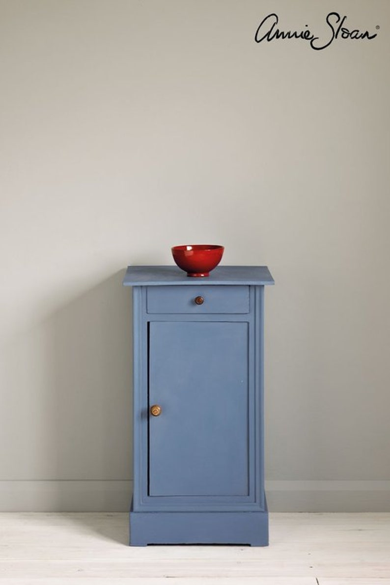 May include: A small blue painted cabinet with a single drawer and a door. The cabinet has a wooden knob on the door and a small red bowl on top.