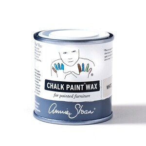 May include: A white tin of Annie Sloan Chalk Paint Wax for painted furniture. The tin features a hand illustration with colorful paint on the fingers. The text on the tin reads "Chalk Paint Wax" and "for painted furniture".