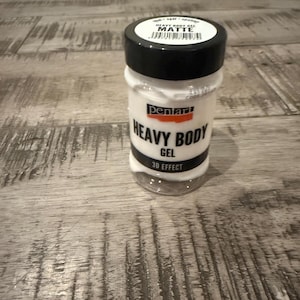 May include: A clear plastic jar of Pentart Heavy Body Gel with a black screw-top lid. The label features the text Pentart, Heavy Body Gel, 3D Effect, and Matte. The jar contains a thick white substance visible through the clear base.