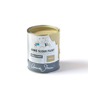 May include: A can of Annie Sloan Chalk Paint in the color Versailles. The paint is a light beige color and is slightly dripped down the side of the can. The can is labeled with the Annie Sloan logo and the name of the color.
