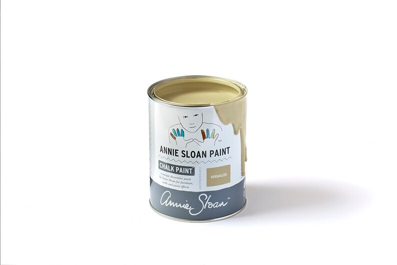 May include: A can of Annie Sloan Chalk Paint in the color Versailles. The paint is a light beige color and is slightly dripped down the side of the can. The can is labeled with the Annie Sloan logo and the name of the color.
