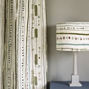 May include: A white lampshade with a green, brown, and blue geometric pattern. The lampshade is on a white lamp base and sits on a blue table with a drawer. The text "Annie Sloan" is visible in the upper right corner of the image.