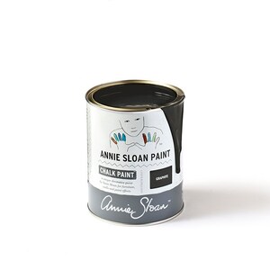 May include: A can of Annie Sloan Chalk Paint in the color Graphite. The can is white with black lettering and a handprint design. The paint is a dark gray color.