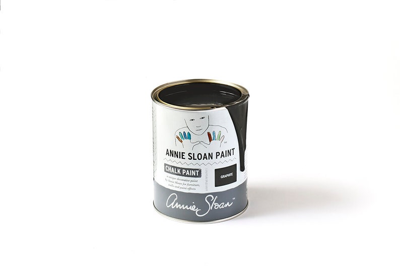 May include: A can of Annie Sloan Chalk Paint in the color Graphite. The can is white with black lettering and a handprint design. The paint is a dark gray color.