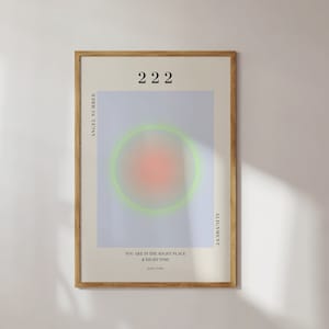 May include: A framed poster with a light blue background and a green and pink circle in the center. The text "2222" is at the top of the poster. The text "Angel Number" is on the left side of the poster. The text "Alignment" is on the right side of the poster. The text "You are in the right place at the right time." is at the bottom of the poster.