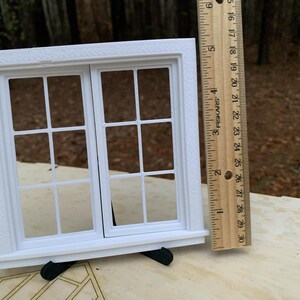 Op de afbeelding: Een wit miniatuurraam met een rechthoekig frame en meerdere ruiten. Het raam wordt ondersteund door zwarte steunen. Een liniaal staat naast het raam en toont de afmetingen in centimeters.