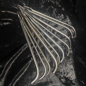 May include: A set of ten silver surgical instruments with curved ends. The instruments are arranged in a fan shape on a black fabric background.