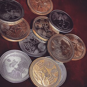 May include: A collection of ten round, metallic coins with various designs and engravings. The coins are in shades of gold, silver, and black. Some of the coins feature intricate designs of birds, stars, and other symbols.