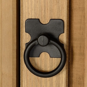 May include: Black metal ring pull handle with a square backplate. The handle is mounted on a wooden door.