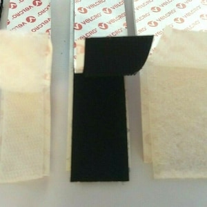 May include: Four strips of black hook and loop fastener tape with adhesive backing. The tape is labelled "VELCRO" and is shown with the adhesive backing exposed.