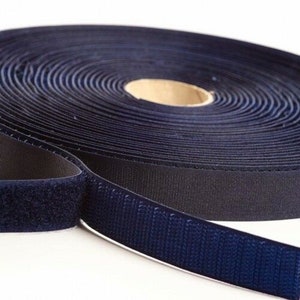 May include: A roll of dark blue hook and loop fastener tape. The tape is rolled up and the hook side is facing out. The loop side is visible on the end of the roll.