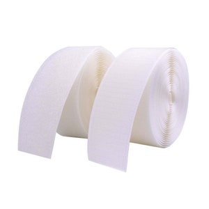 May include: Two rolls of white hook and loop tape, also known as Velcro, are shown. The tape is rolled up and the ends are unrolled, showing the texture of the fabric.
