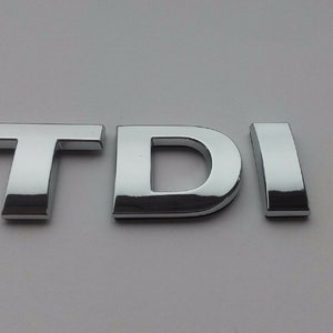 May include: Chrome-plated metal letters spelling out "TDI" on a white background.