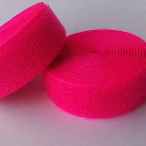 May include: Two rolls of bright pink hook and loop fastener tape. The tape is rolled up and ready to be used for crafts, sewing, or other projects.