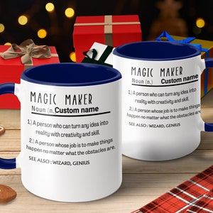 May include: White ceramic coffee mug with a blue rim. The mug features a definition of "Magic Maker" with the text "Custom name" in place of the definition. The text reads: "Magic Maker Noun (n.) Custom name 1. A person who can turn any idea into reality with creativity and skill. 2. A person whose job is to make things happen no matter what the obstacles are. See also: Wizard, Genius."